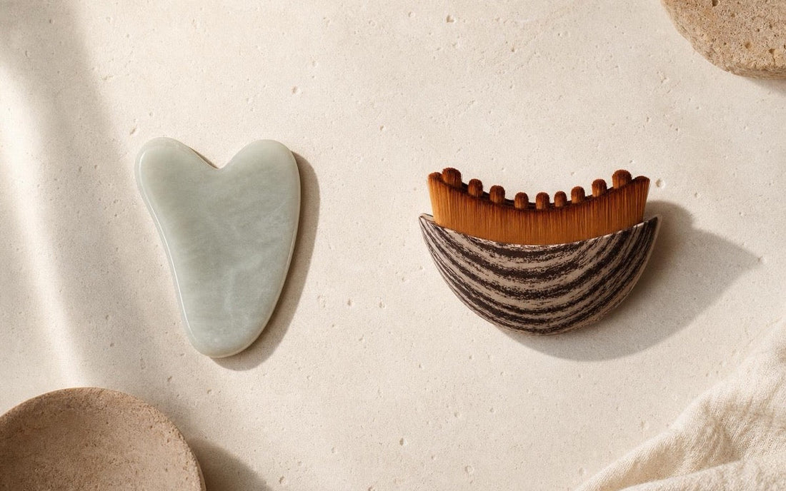 A polished gua sha stone beside the Sanamar Contour brush, photographed from above on cream stone