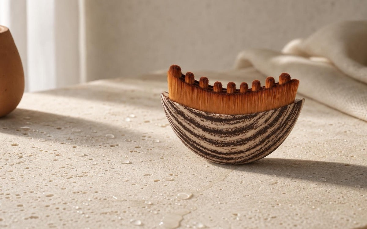 The Sanamar Contour lymphatic brush on a cream stone surface scattered with clear water droplets